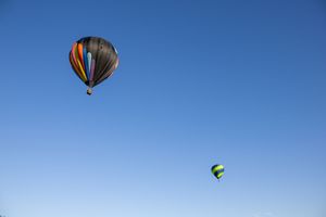 Multiple hot air balloons floating in distance against clear blue sky.