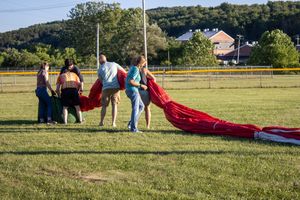 People setting up hot air balloon equipment in a grassy field during sunset.