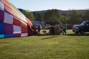 Colorful hot air balloon being set up on a grassy field with vehicles and crew members nearby.