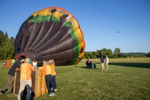 A large deflated hot air balloon being prepared for launch in a sunny field.