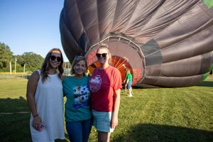Group standing in front of a partially inflated hot air balloon on a grassy field.