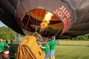 Hot air balloon burners igniting during evening setup with crew members in green shirts.