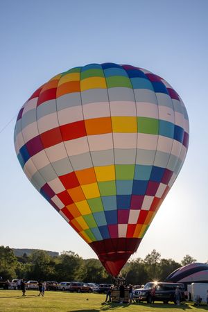 Vibrant rainbow-colored hot air balloon inflated against blue sky with spectators below.