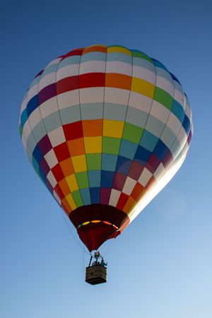Rainbow-checkered hot air balloon floating in bright blue sky.