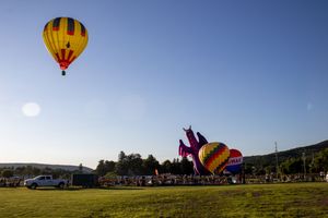 Yellow hot air balloon and inflatable figure silhouetted against late afternoon sky.