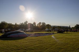 Sun setting over a hot air balloon festival field with parked cars.