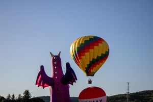 Colorful hot air balloons floating against a bright blue sky with a purple inflatable figure visible below.