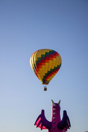 Hot air balloon with vibrant rainbow stripes ascending in the clear blue sky.