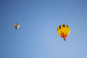 Multiple hot air balloons soaring in a bright blue sky during a balloon festival.