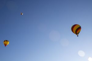 Several hot air balloons floating high in the blue sky with sun flare visible.