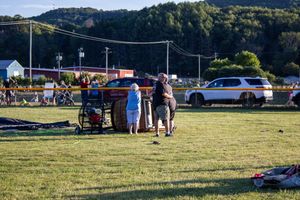 Panoramic view of a grassy field with parked cars and festival attendees.