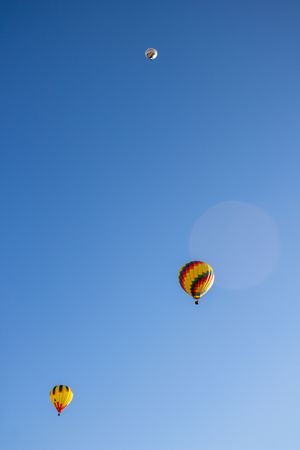 Hot air balloons with yellow and red patterns floating against clear blue skies.