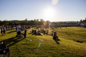 Golden sunset light illuminates a grassy hillside where festival attendees gather.