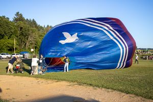 Blue and white striped hot air balloon being inflated on the ground at a festival.