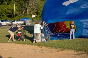 Large blue hot air balloon being prepared for launch in a grassy field.
