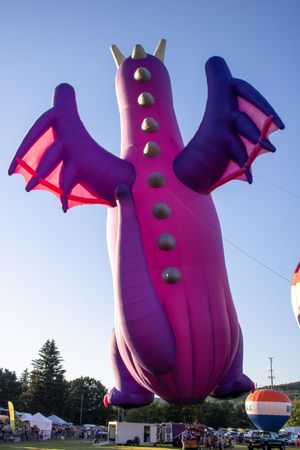 Large purple inflatable character with green buttons rises against blue sky at outdoor event.