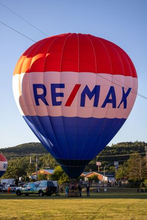 RE/MAX hot air balloon in red white and blue colors being inflated on grassy field.