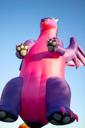 Close-up view of purple and pink inflatable character balloon against bright blue sky.