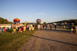 Wide view of hot air balloon festival grounds with multiple balloons and attendees at sunset.
