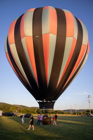 Orange and brown striped hot air balloon being prepared for launch at outdoor festival.