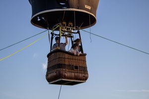 Hot air balloon basket suspended by cables against clear blue sky.
