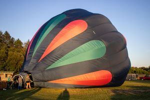 Hot air balloon being inflated on a grassy field at sunset with colorful red, green and black panels.
