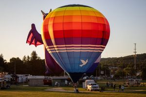 Large rainbow-colored hot air balloon envelope being set up in a field during golden hour.