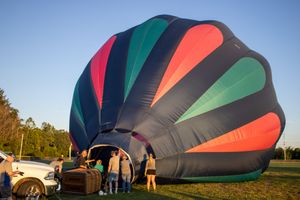 Hot air balloon with vibrant red, green and black panels being prepared for flight at dusk.