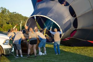 Crew members working together to set up and inflate a large hot air balloon on a grassy field.