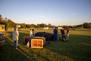 Hot air balloon preparation site with equipment and vehicles spread across an open field at sunset.