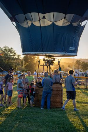 Spectators gather around hot air balloon baskets at sunset during a balloon festival.