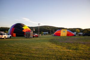 Multiple hot air balloons scattered across a grassy field during a festival at sunset.