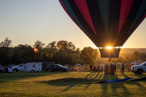 Hot air balloons silhouetted against a vibrant sunset sky during a summer festival.