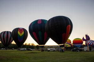 Row of hot air balloons being inflated on a grassy field at sunset.