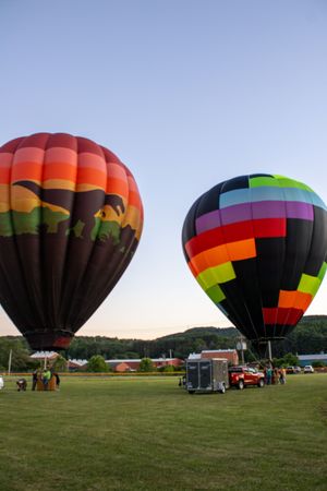 Colorful striped hot air balloons standing ready for takeoff in a grassy field.