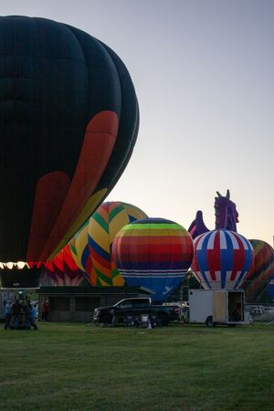 Colorful hot air balloons lined up on a grassy field during a balloon festival at sunset.