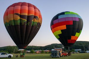 Row of vibrant hot air balloons preparing for takeoff in an open field at dawn.