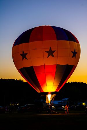 Hot air balloon glowing orange against a darkening sky during a nighttime balloon glow event.