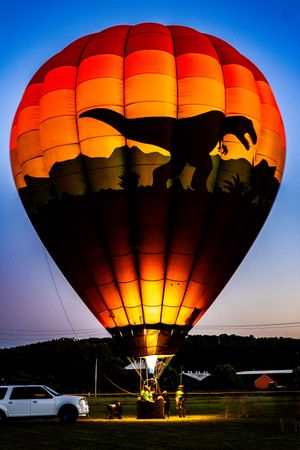 Hot air balloon silhouetted against evening sky with crew preparing for flight.