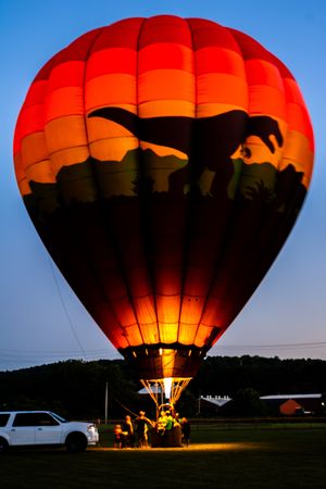 Large red hot air balloon illuminated from within against a blue twilight sky.