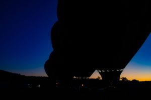 Dark silhouettes of multiple hot air balloons against a deep blue evening sky.