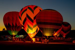 Hot air balloons glowing bright red and orange during a nighttime balloon glow event.