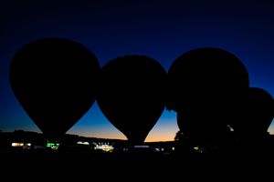 Silhouettes of multiple hot air balloons at dusk with fading sunlight in background.