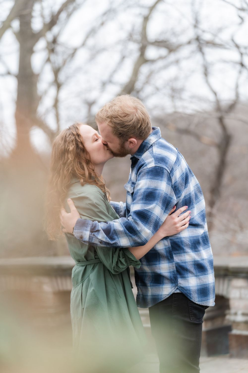 Tender kiss shared on a balcony overlooking early spring woods during a March engagement session in Chaska, MN