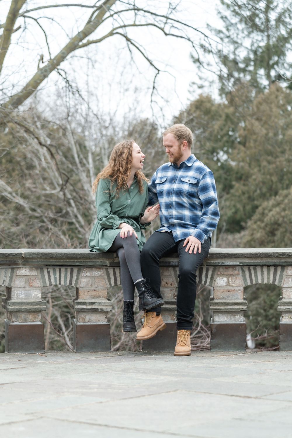 Engaged couple embracing on a stone balcony with bare trees in the background at the Minnesota Landscape Arboretum