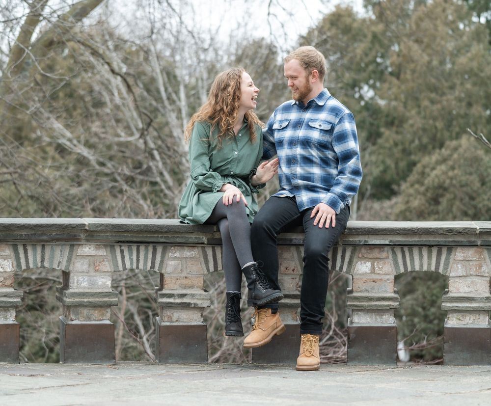 Couple smiling at each other while standing under a tree just starting to bud in early March