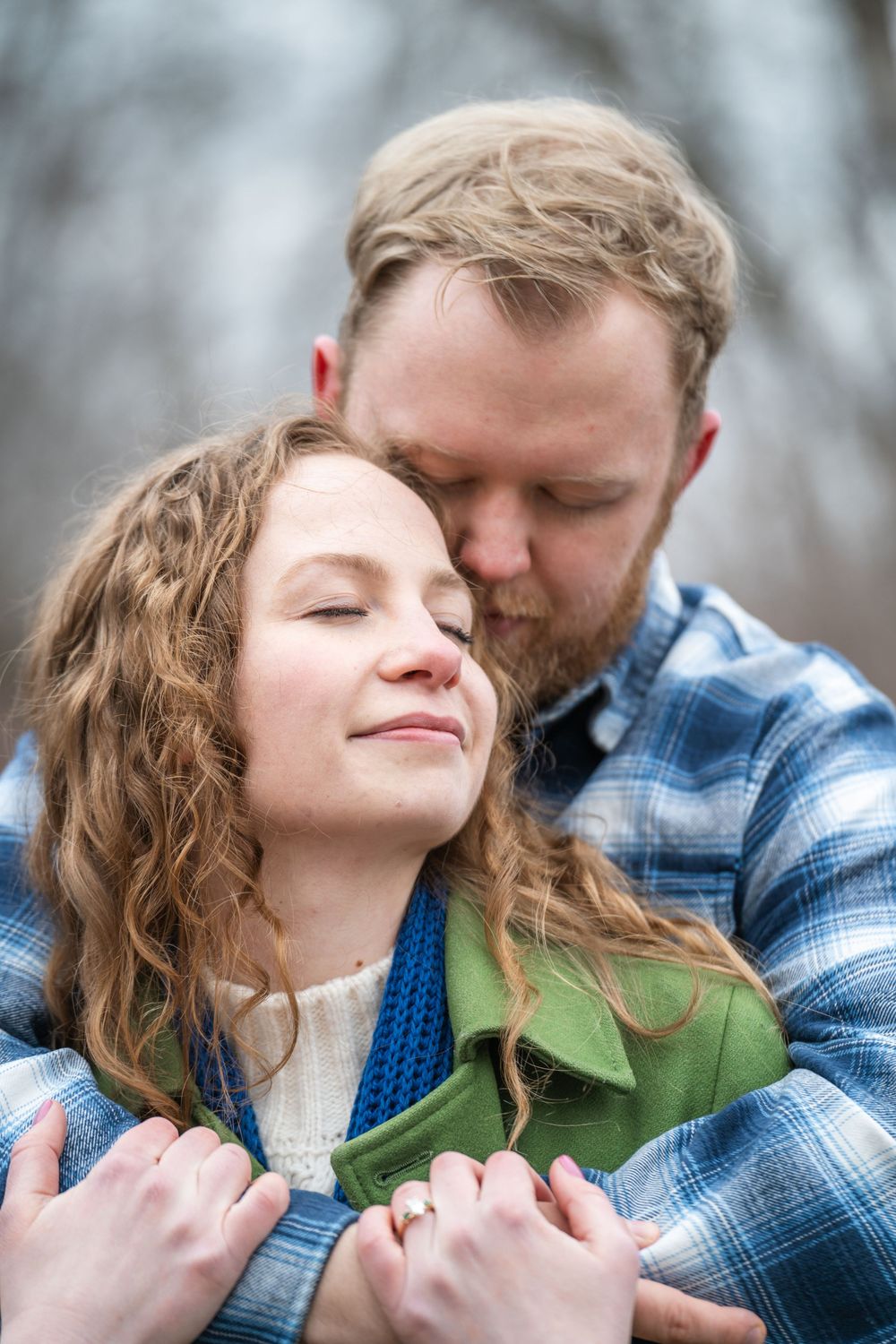 Bride-to-be leaning into her fiancé with a soft smile as spring buds bloom around them