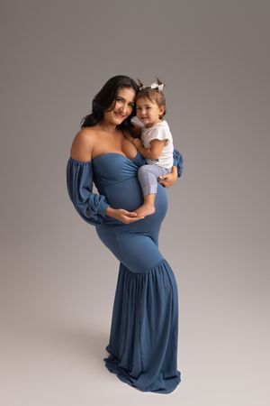 Maternity photo series showing tender moments in blue dress against grey backdrop, showcasing elegant curves and motherhood.