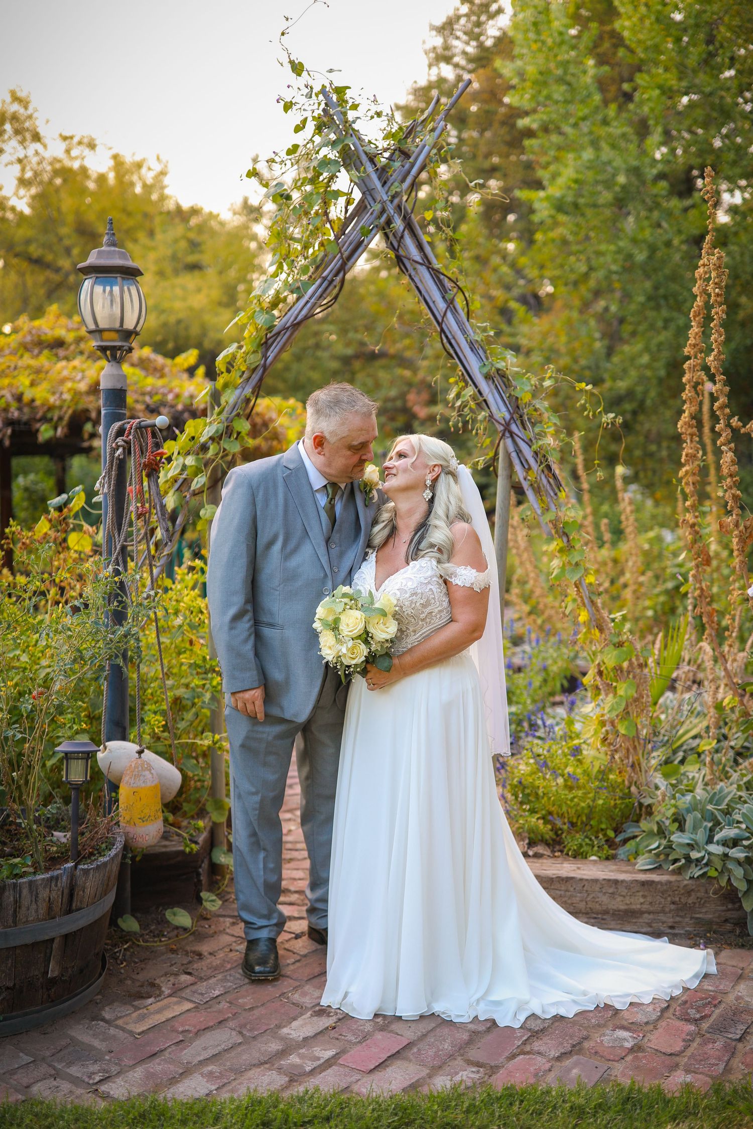 Wedding couple sharing romantic moment in garden pathway with lantern lighting.