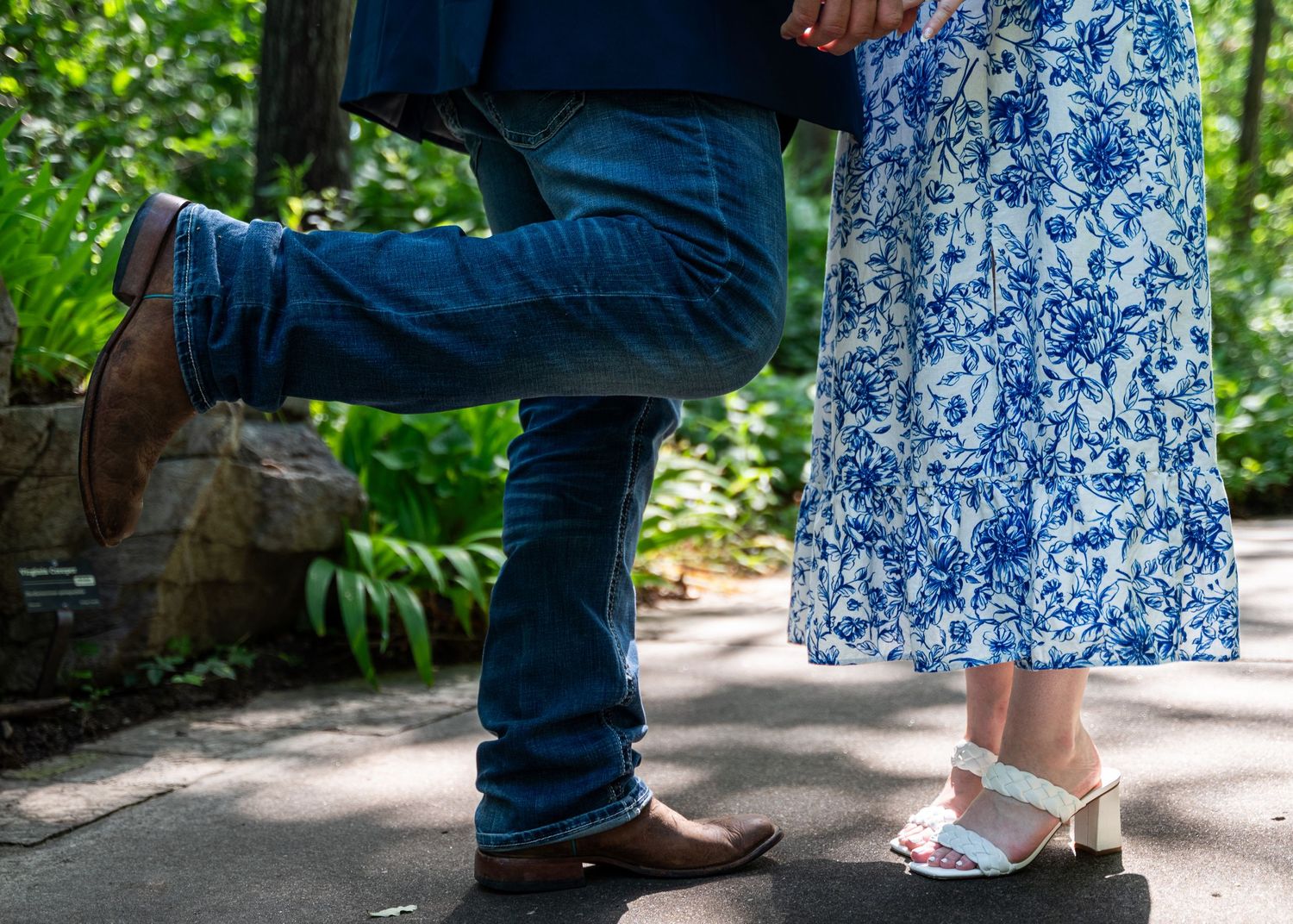 Waist down view of couple, man wearing jeans and cowboy boots with one foot popped in the air, woman wearing blue and white dress